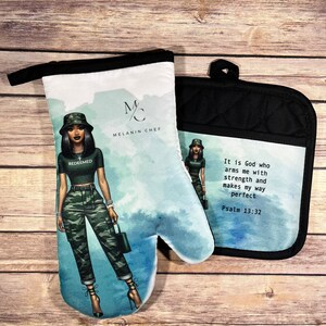 May include: A set of two oven mitts featuring a woman in a camouflage outfit with the text "REDEEMED" on her shirt. The larger mitt has a watercolor background and the text "MELANIN CHEF". The smaller mitt has the text "It is God who arms me with strength and makes my way perfect Psalm 13:32".