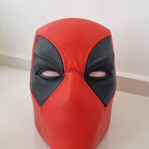 Könnte beinhalten: Rote und schwarze Deadpool-Maske mit strukturierter Oberfläche. Die Maske hat eine schwarze Augenmaske mit weißen Augen.