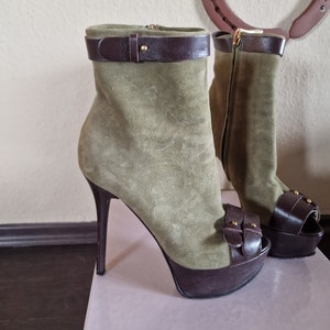 Könnte beinhalten: Ein Paar grüne Wildleder-Plateau-Heels mit braunen Lederriemen und Schnallen. Die Absätze sind etwa 12,7 cm hoch und haben eine offene Zehenpartie.