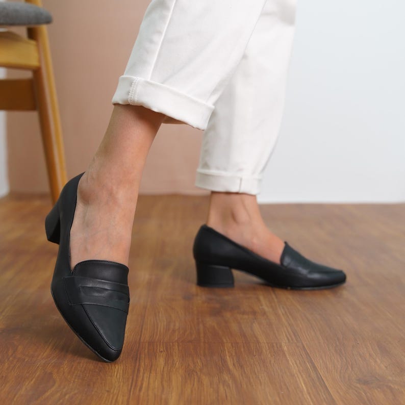 Side view of a woman walking in black vegan leather bridal block low heel loafers, showcasing the sleek and stylish design hyl wedding short heels.