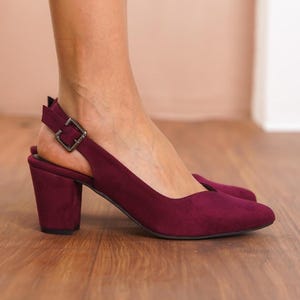 May include: Burgundy suede heeled slingback shoes with a buckle closure. The shoes have a block heel and a pointed toe.