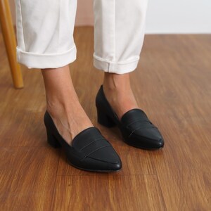 Front view of a woman standing in black vegan leather low block heel loafers, capturing the sophisticated look and sleek design hyl wedding short heels.