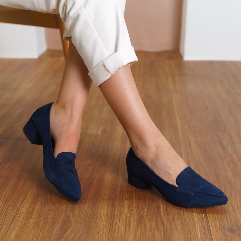 Top down flat lay of two navy blue vegan suede loafers, showcasing the elegant pointed toe design and contrasting sturdy low block heels, arranged on a neutral background.
