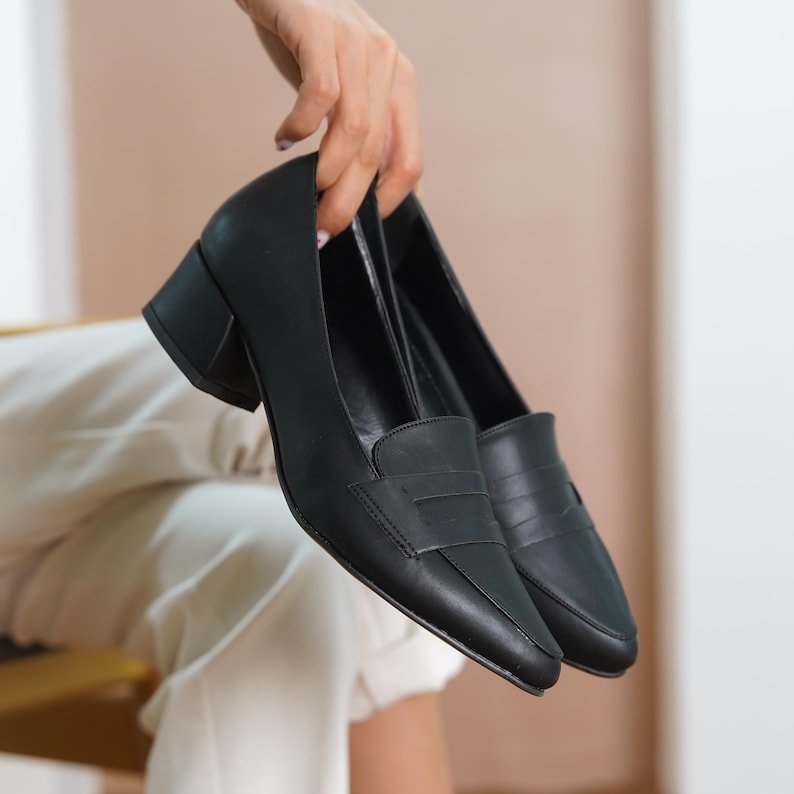 A hand holding black vegan leather block low heel loafers, displaying the chic and elegant style of the hyl wedding short shoes.