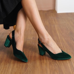 Close-up view of elegant green silky velvet slingback medium high block Hyl Wedding heels on a wooden floor.