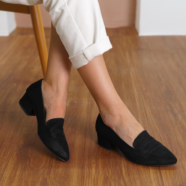 Top down flat lay of two black vegan suede loafers, showcasing the elegant pointed toe design and contrasting sturdy low block heels, arranged on a neutral background.