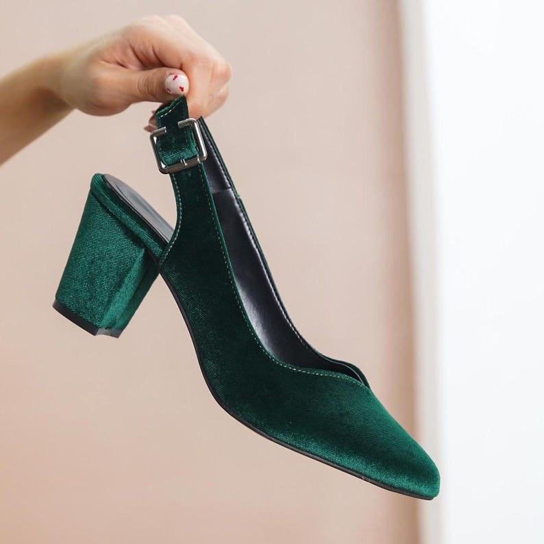 Hand holding a pair green silky velvet slingback block Hyl Wedding heel, showing the shoes elegant style and quality craftsmanship.