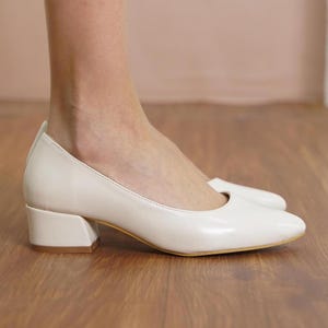 May include: A pair of off-white low heeled pumps with a square toe and a block heel.