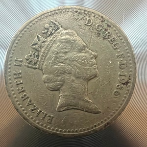 May include: A silver coin featuring a profile of Queen Elizabeth II with the inscription "D.G. REG. F.D. 1980" around the edge.