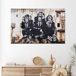 May include: A framed print depicting a black and white mural of three chimpanzees in suits. One covers its ears, another its eyes, and the third its mouth. The background is a rusty metal surface.