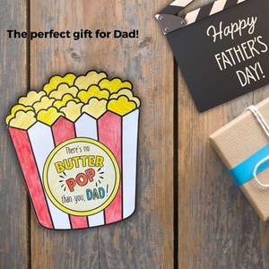 May include: A colorful, hand-drawn popcorn box with the text "There's no BUTTER POP than you, DAD!" on a yellow circle. A black clapperboard with "Happy FATHER'S DAY!" and a wrapped gift with a blue ribbon are also visible.