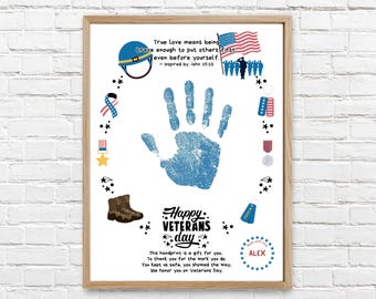Op de afbeelding: Een ingelijste print met een centrale blauwe handafdruk omringd door militaire illustraties, waaronder een helm, Amerikaanse vlag, dogtags en laarzen. De tekst luidt: True love means being brave enough to put others first, Happy Veterans Day.