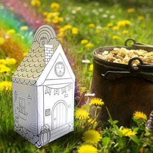 May include: A white papercraft house with a green shamrock on the window, a rainbow on the roof, and a pot of gold in front of it. The house is sitting in a field of green grass and yellow dandelions.