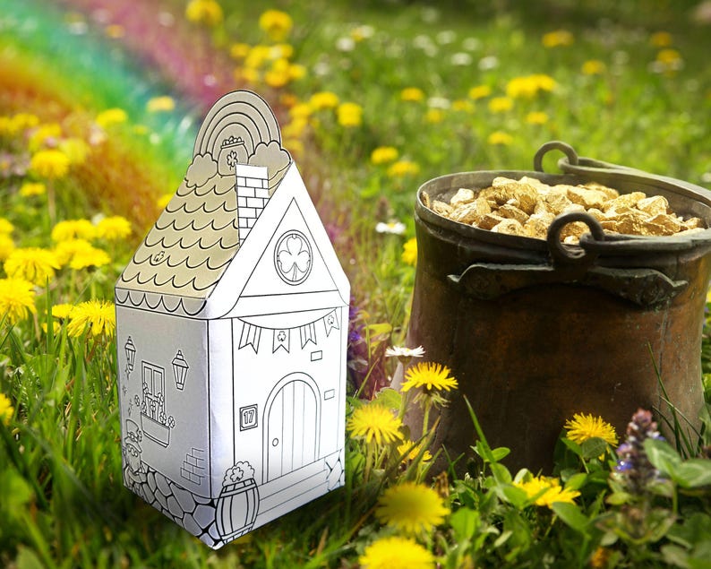 May include: A white papercraft house with a green shamrock on the window, a rainbow on the roof, and a pot of gold in front of it. The house is sitting in a field of green grass and yellow dandelions.