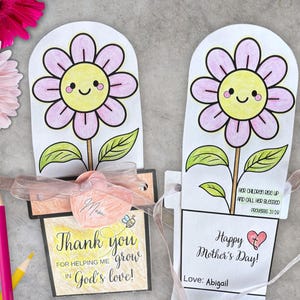 Op de afbeelding: Twee handgemaakte Moederdagkaarten met bloemontwerpen. Eén kaart zegt "Bedankt dat je me hebt geholpen te groeien in Gods liefde!" en de andere zegt "Fijne Moederdag!" met een hart. De kaarten zijn vastgebonden met linten.