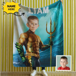 Puede incluir: Una manta de forro polar personalizada con un ni&ntilde;o vestido como Aquaman, sosteniendo un tridente. La manta tiene un dise&ntilde;o de ola de mar azul y verde y el nombre "LIAM" impreso en ella.