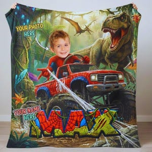 May include: A personalized blanket featuring a child's photo in a Spider-Man costume driving a red monster truck. The design includes a T-Rex, a pterodactyl, and the name "MAX" in a comic book style. The text "YOUR PHOTO HERE" and "YOUR NAME HERE" are also visible.