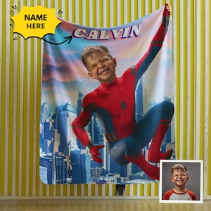 Puede incluir: Una manta de forro polar personalizada con la cara de un ni&ntilde;o superpuesta al cuerpo de Spiderman, con el nombre "CALVIN" impreso en la parte superior. La imagen muestra a Spiderman balance&aacute;ndose por un paisaje urbano.