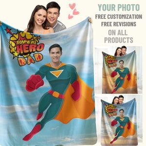 Puede incluir: Una manta de franela azul y blanca con un dise&ntilde;o de superh&eacute;roe. El dise&ntilde;o presenta a una persona con un traje de superh&eacute;roe verde y naranja con el texto "Super Hero Dad" en rojo y amarillo.