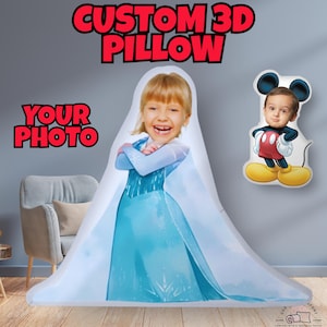 Op de afbeelding: Een wit 3D-kussen met een aangepaste foto van een meisje dat verkleed is als Elsa uit Frozen. Het kussen ligt op een witte fauteuil. De tekst "CUSTOM 3D PILLOW" staat in rode letters boven het kussen. De tekst "YOUR PHOTO" staat in rode letters links van het kussen.