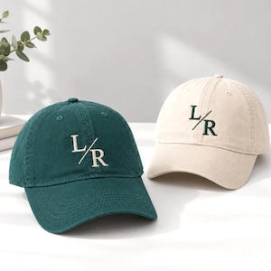 Pode incluir: Um boné de beisebol verde-escuro com texto L/R bordado em branco e um boné bege com texto L/R bordado em verde-escuro. Ambos os bonés apresentam uma construção de seis painéis, uma aba curva e um botão no topo da coroa.