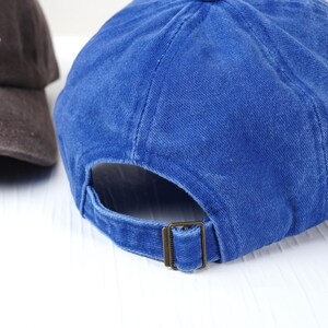 May include: Two baseball caps. One is a deep blue, the other is brown. The blue cap has a metal buckle closure. The brown cap has white text. Both caps are made of a soft, textured fabric.
