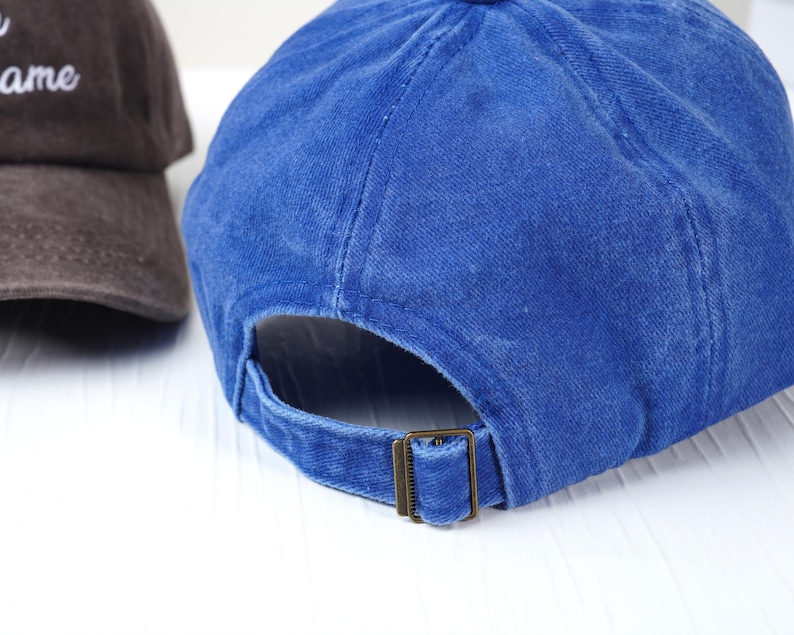 May include: Two baseball caps. One is a deep blue, the other is brown. The blue cap has a metal buckle closure. The brown cap has white text. Both caps are made of a soft, textured fabric.