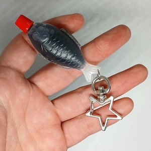 Pu&ograve; includere: Un portachiavi originale con una bottiglia di salsa di soia a forma di pesce con tappo rosso. La bottiglia grigio scuro ha un motivo a squame di pesce ed &egrave; attaccata a un ciondolo a forma di stella argentata.