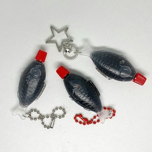 3 soy sauce fish bottles with red caps filled with black liquid showing 3 keyring options including a star-shaped keyring, a silver ball chain, and a red ball chain.
