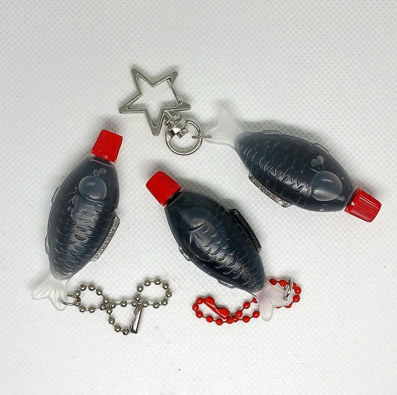 3 soy sauce fish bottles with red caps filled with black liquid showing 3 keyring options including a star-shaped keyring, a silver ball chain, and a red ball chain.