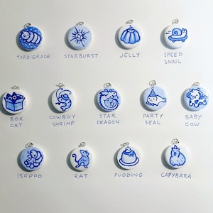 May include: Twelve blue and white ceramic ornaments with different animal and object illustrations. Each ornament has a silver loop for hanging. The ornaments are arranged in three rows of four.