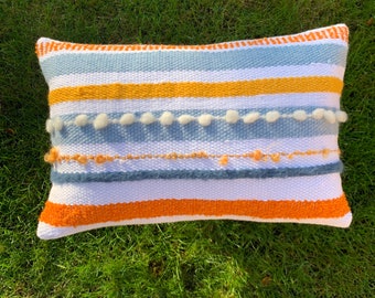 Housse de coussin tactile texturée tissée à la main dans une belle palette de couleurs bleues, blanc orangé. Soutenu par une fermeture à bouton blanc en laine bleue.