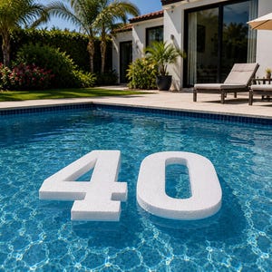 May include: Large white foam numbers four and zero floating on the surface of a blue swimming pool. The numbers are positioned in the center of the water, creating a clear display of the number forty against the rippling blue pool water.