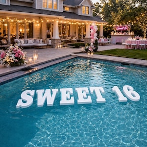 May include: Large white floating letters spelling SWEET 16 are positioned in a backyard swimming pool. The pool area features a patio with outdoor seating, string lights, pink and white balloon clusters, and tables set for an evening event.
