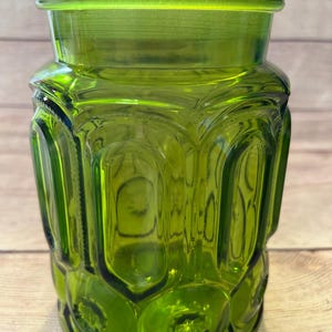 Op de afbeelding: Een groene glazen pot met een deksel. De pot heeft een sterrenpatroon en een cilindrische vorm. De pot van transparant groen glas staat op een houten oppervlak.