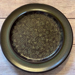 May include: A dark brown dinner plate with a green rim and a green floral pattern.