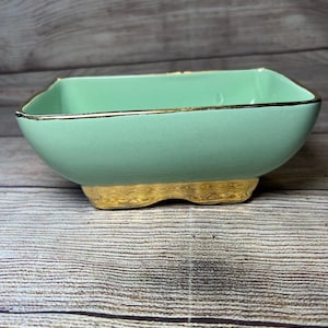 以下が含まれることがあります： 金色の縁取りと波打つ金色の底を持つ、正方形の薄い緑色のセラミックボウルです。