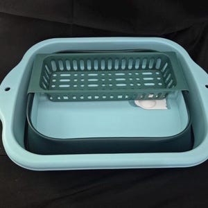 May include: A light blue collapsible dish drying rack with a dark green basket insert. The rack has a rectangular shape with rounded corners and handles. A dark blue basin is inside the rack.