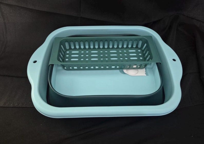 May include: A light blue collapsible dish drying rack with a dark green basket insert. The rack has a rectangular shape with rounded corners and handles. A dark blue basin is inside the rack.