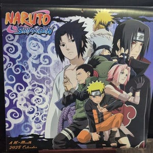 May include: A 2025 calendar featuring characters from the anime series Naruto Shippuden. The cover displays a group of characters in various poses, with the series title in a colorful font. The background has a pattern of blue swirls.