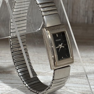 May include: Silver-toned Pulsar watch with a rectangular black face. The watch features a stretch band and is displayed on a clear stand. The watch face has silver hands and the brand name "PULSAR" is printed on the face.