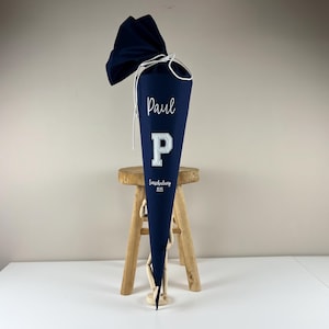 Könnte beinhalten: Ein dunkelblauer Schultüte mit weißer Beschriftung. Die Tüte ist mit dem Namen "Paul" und dem Buchstaben "P" verziert.
