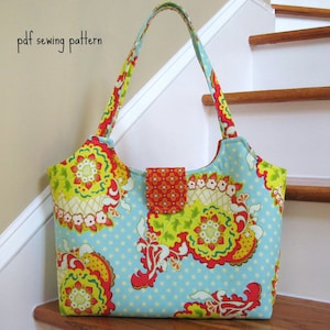 May include: A blue and white tote bag with a floral pattern and a red and orange flap closure. The bag has a pdf sewing pattern.