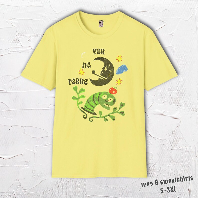 May include: Yellow t-shirt with a whimsical graphic featuring a smoking crescent moon, a green worm, and the text "VER DE TERRE". The design includes stars, a cloud, and an apple. The shirt is part of a collection of tees and sweatshirts, sizes S-3XL.