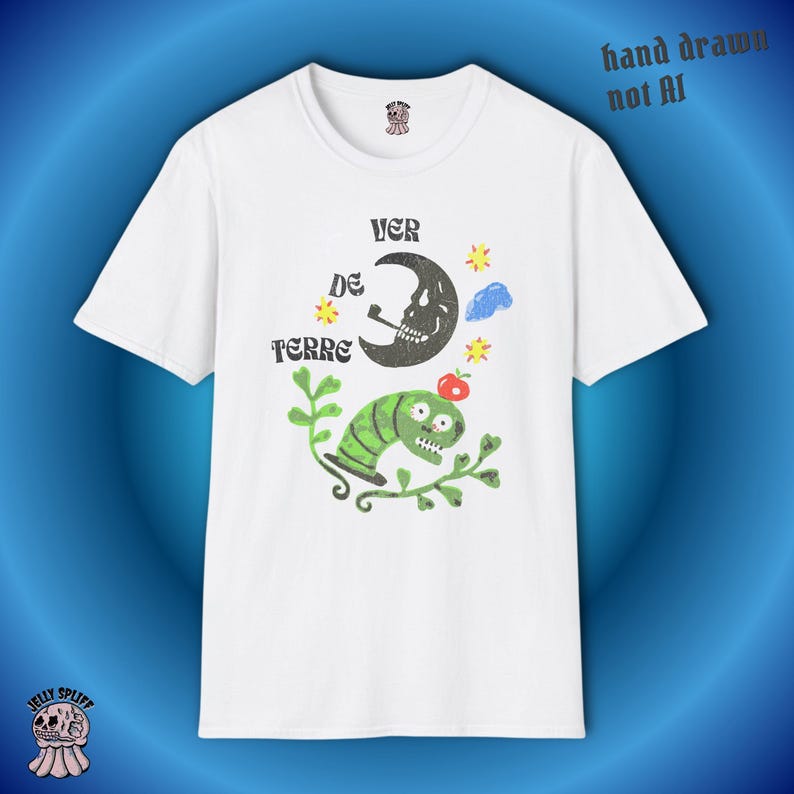 May include: White t-shirt with a whimsical graphic featuring a smoking skull moon, a green caterpillar, and the text "VER DE TERRE." The design includes stars, a cloud, and a red apple. The words "hand drawn not AI" are printed on the top right.