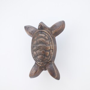 Pu&ograve; includere: Statuetta di tartaruga color bronzo con pinne estese. Il guscio della tartaruga presenta un motivo strutturato e dettagliato. La statuetta &egrave; probabilmente in metallo e si trova su uno sfondo bianco.