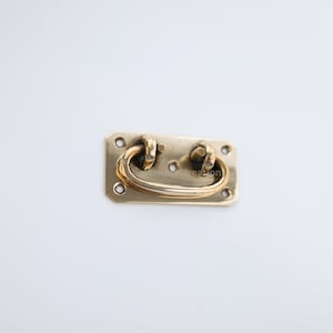 May include: A gold-toned metal drawer pull with a rectangular base and a curved handle. The pull has four small holes on the base.