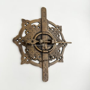 以下が含まれることがあります： 装飾的な複雑なデザインが施された真鍮製のドアのラッチ。ラッチは円形で、十字形のバーとチェーンが付いています。