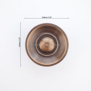 Puede incluir: Un pomo de armario circular de color bronce con un centro elevado y un dise&ntilde;o acanalado. El pomo mide 3,5 cm de di&aacute;metro y 3,5 cm de profundidad. El pomo es un elemento de ferreter&iacute;a decorativo.