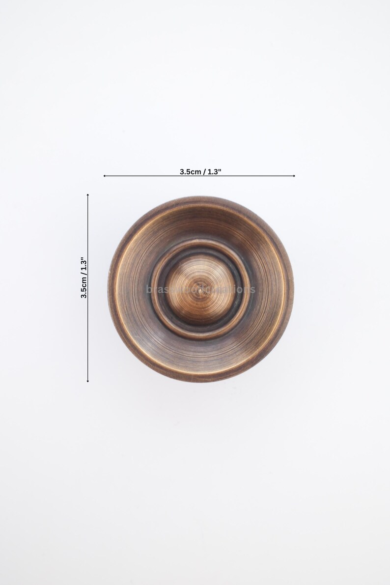 Puede incluir: Un pomo de armario circular de color bronce con un centro elevado y un dise&ntilde;o acanalado. El pomo mide 3,5 cm de di&aacute;metro y 3,5 cm de profundidad. El pomo es un elemento de ferreter&iacute;a decorativo.